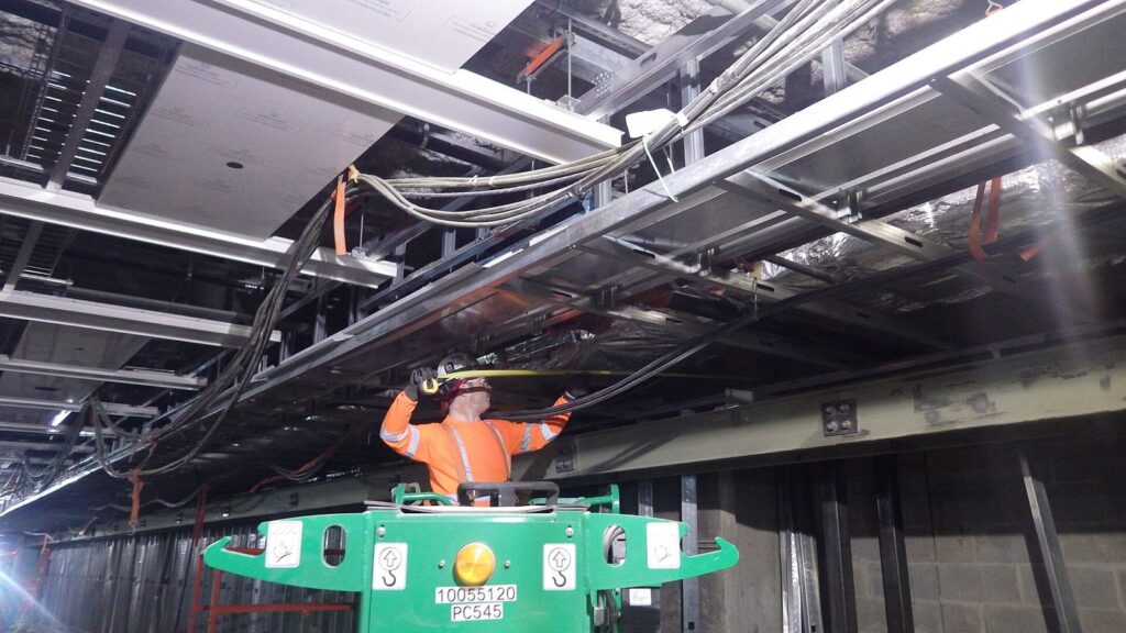 Trabalhador em plataforma elevatória instalando estrutura de forro em área coberta